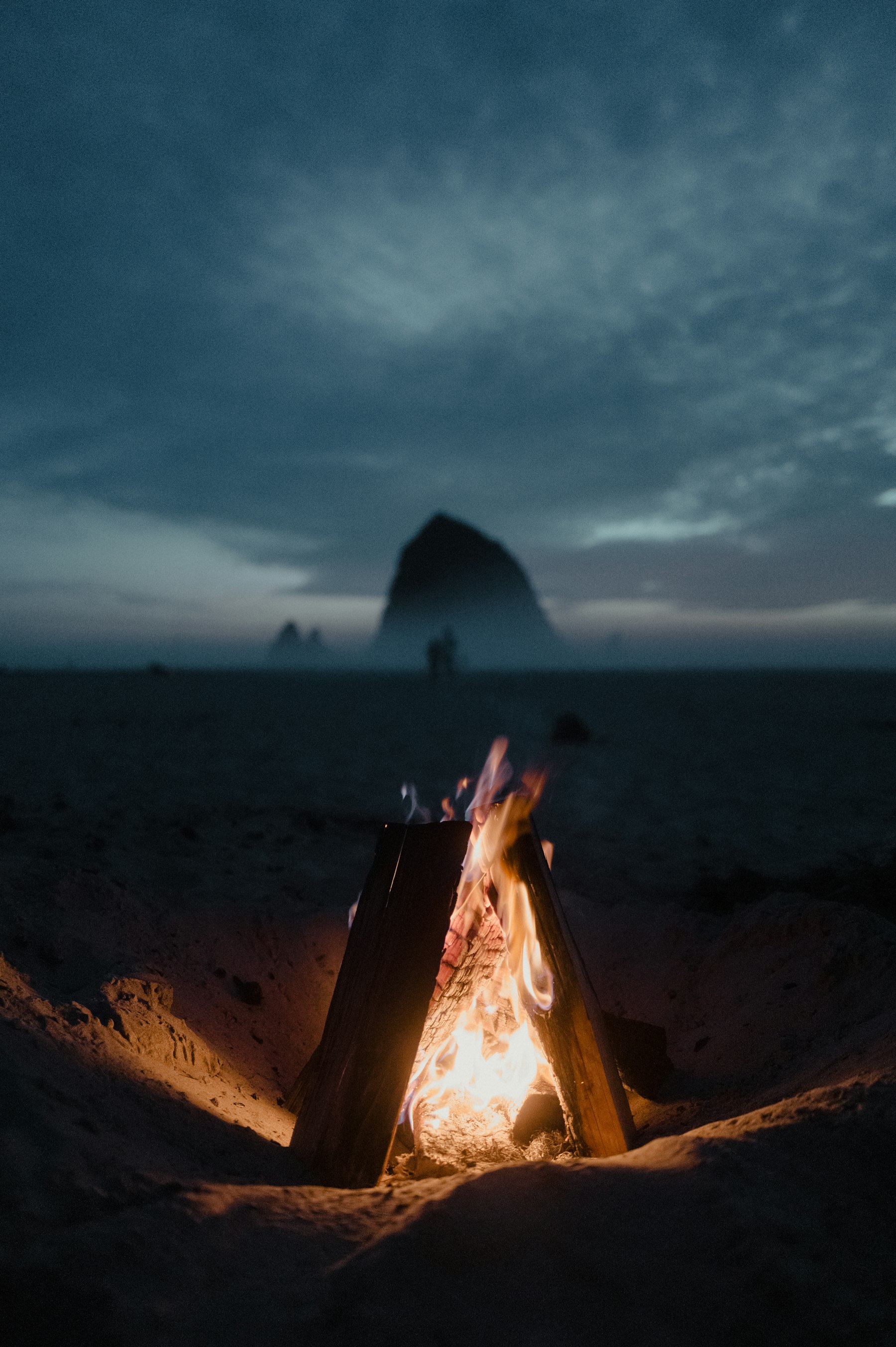A beach fire glowing at dusk beside the surf