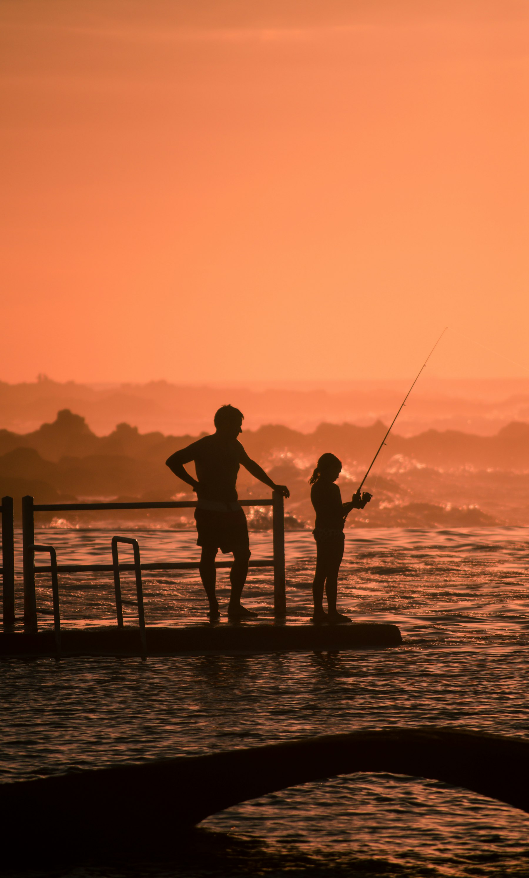 A father and daughter fishing in silhouette at sunset