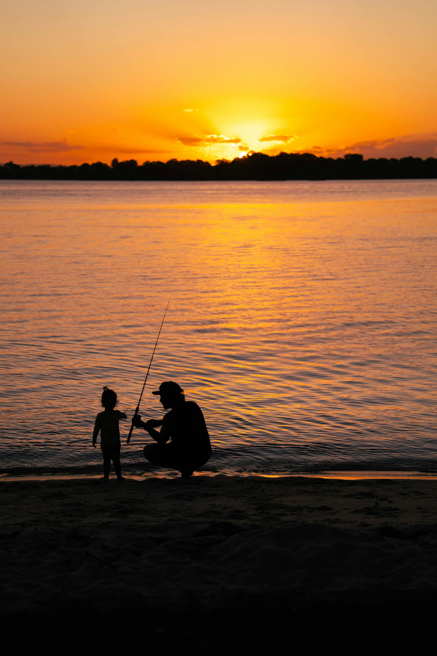 A father teaching his toddler to fish at sunset