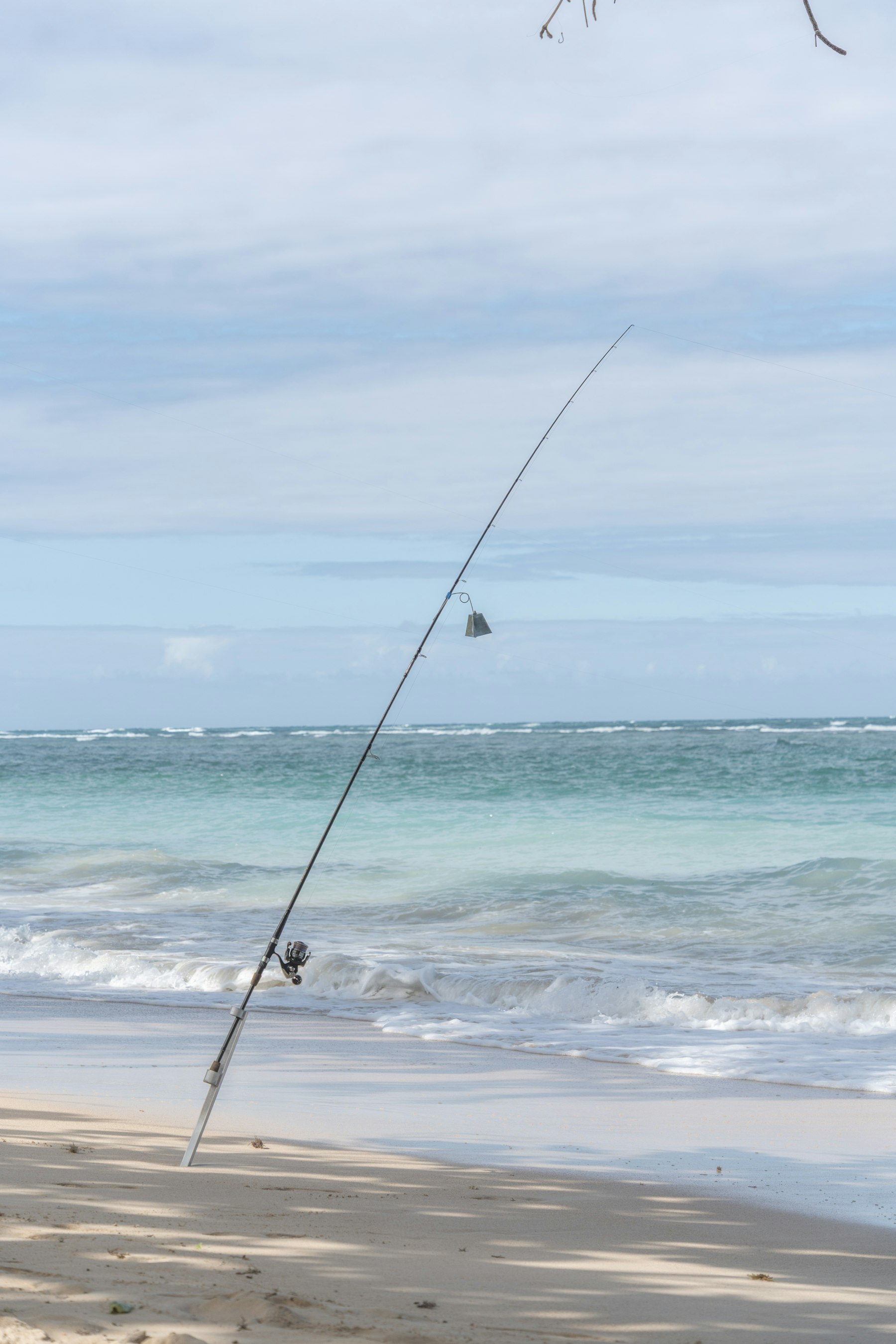 A surf rod standing in a sand spike with a bite bell, waves behind it